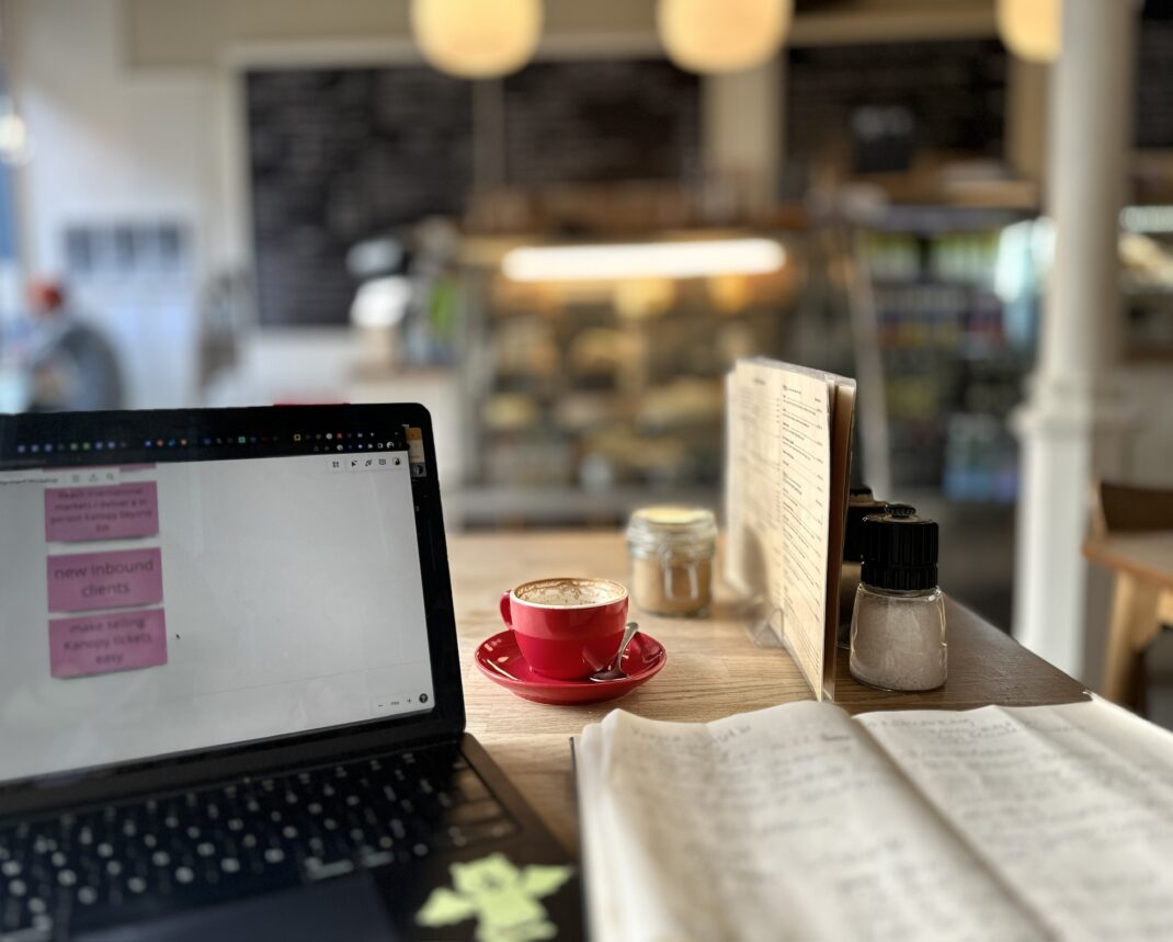 Mac laptop, open notebook and full red cup of coffee in a cafe.